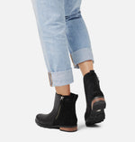 Load image into Gallery viewer, Rear view of female model wearing black 2 tone winter boot. Made of leather and suede and has a zipper. Heel made of wood is also visible.
