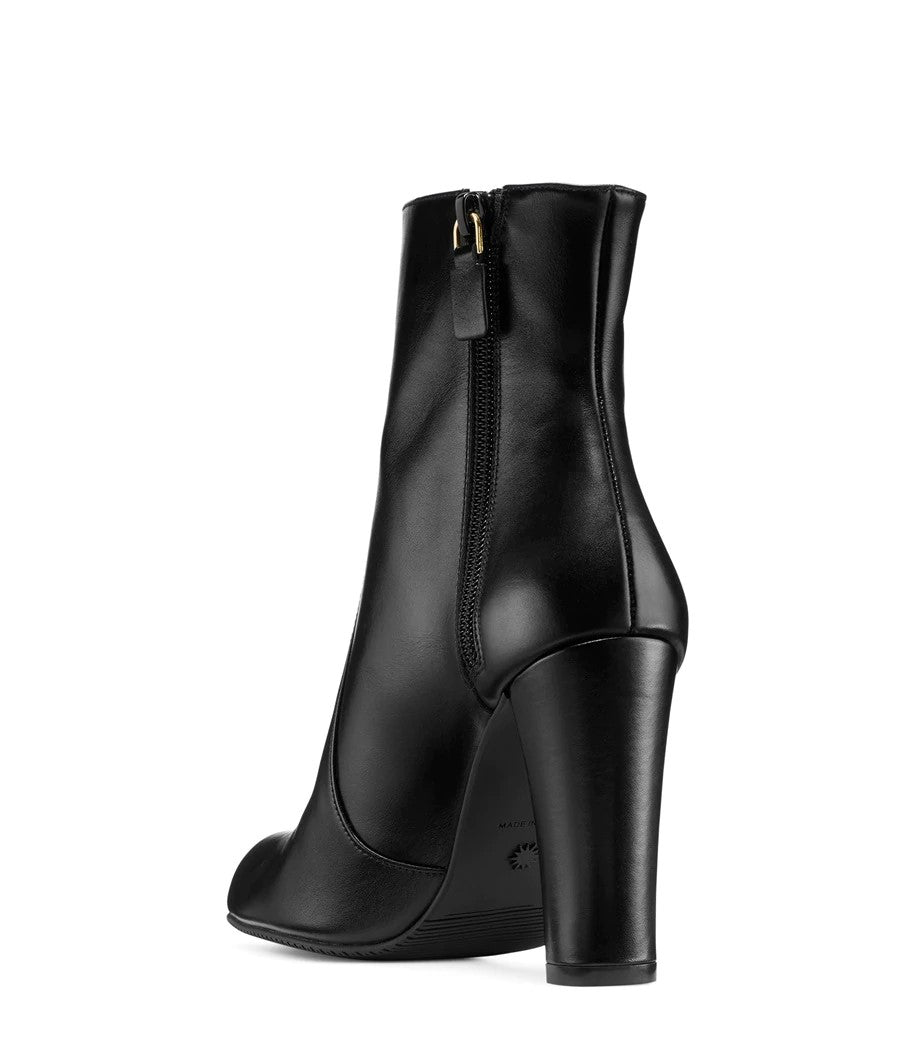 Rear left view of glossy black leather boot. Heel and a zipper on the boot are visible.