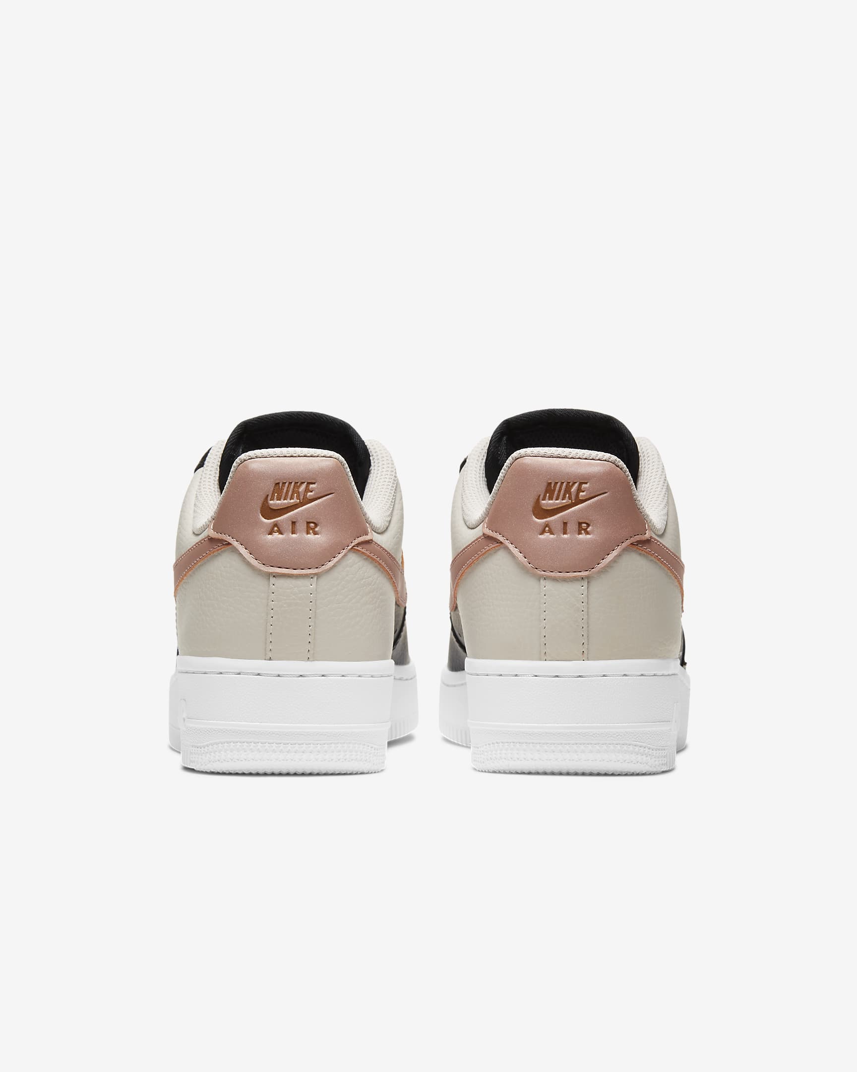 Rear view of Nike shoe. Has white midsole, pink Nike Air inscription and is made of beige leather.